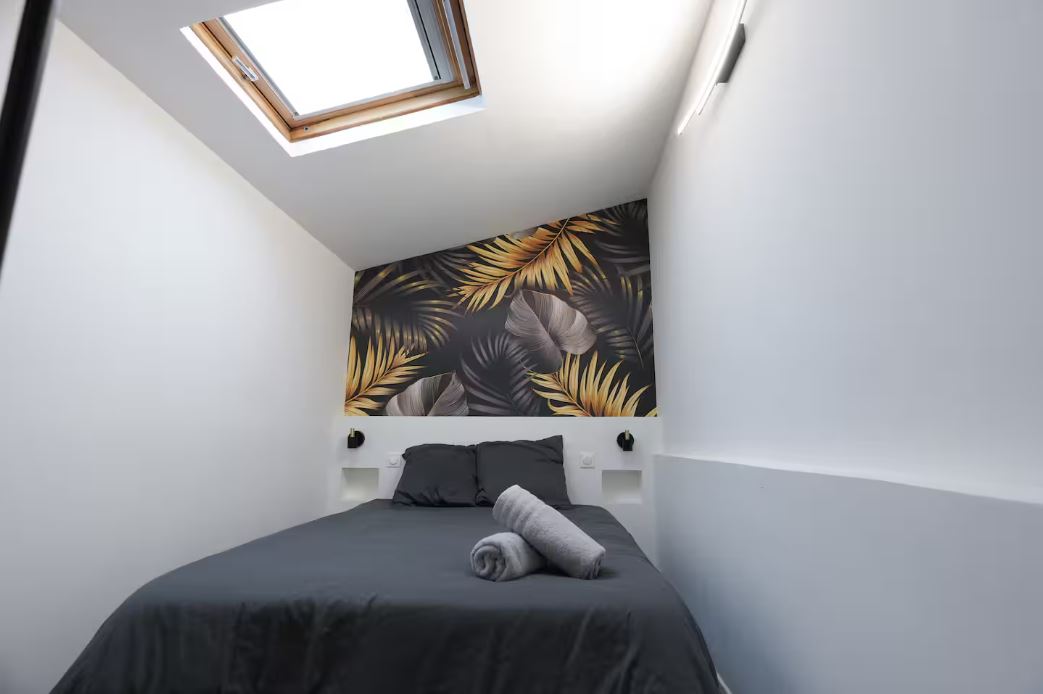 Chambre avec lit double sous velux et papier peint tropical